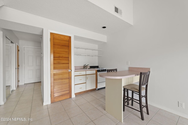 kitchen with white cabinetry, light tile patterned floors, a kitchen bar, kitchen peninsula, and sink