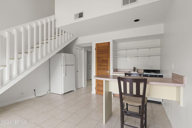 kitchen with white cabinets, white refrigerator, sink, light tile patterned floors, and a breakfast bar area