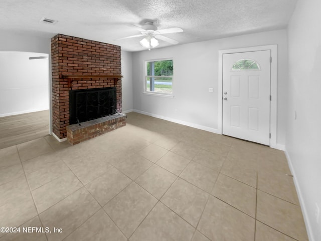 unfurnished living room with ceiling fan, light tile patterned flooring, a textured ceiling, and a fireplace