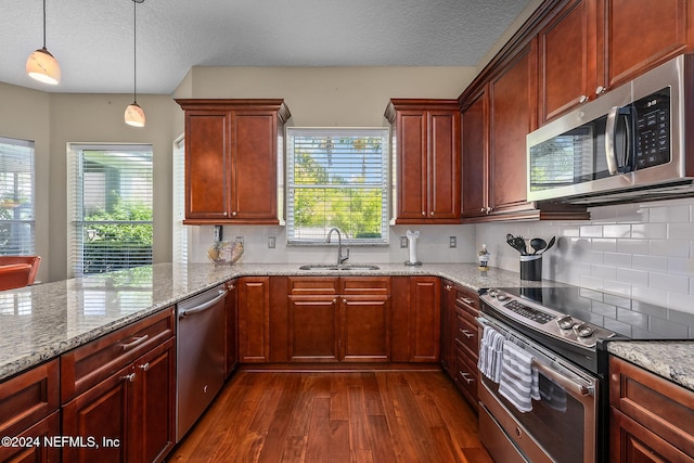 kitchen with pendant lighting, dark wood-type flooring, sink, light stone countertops, and appliances with stainless steel finishes