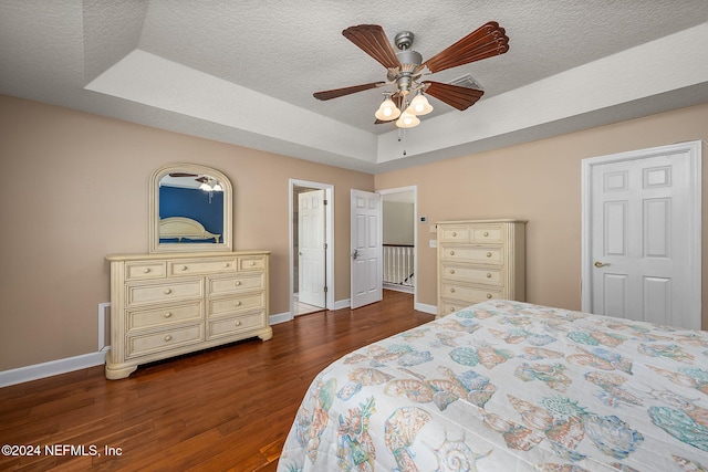 bedroom with ceiling fan, dark hardwood / wood-style floors, a raised ceiling, and a textured ceiling