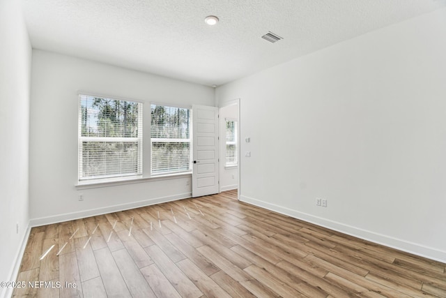 unfurnished room featuring a textured ceiling, baseboards, visible vents, and light wood-style floors