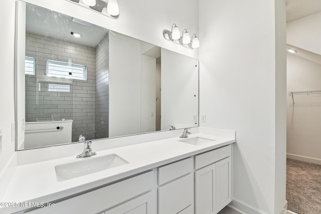 full bathroom featuring a sink, a tile shower, baseboards, and double vanity