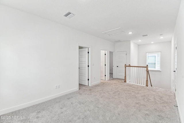 carpeted spare room with attic access, visible vents, and baseboards