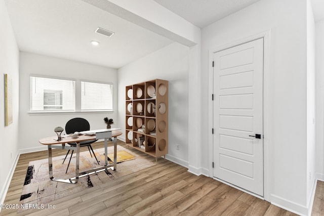 office space with light wood-type flooring, visible vents, and baseboards