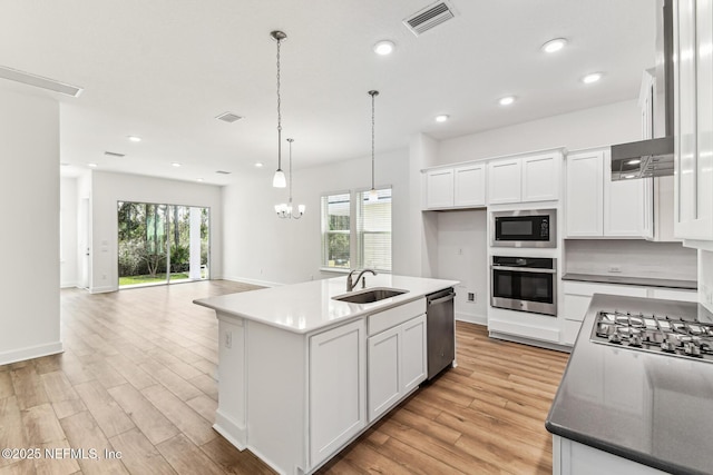 kitchen with stainless steel appliances, a sink, white cabinets, light wood finished floors, and plenty of natural light