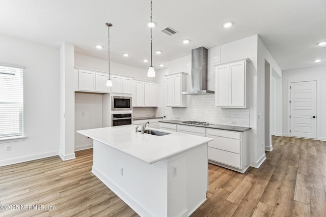 kitchen with a kitchen island with sink, stainless steel appliances, a sink, visible vents, and wall chimney exhaust hood