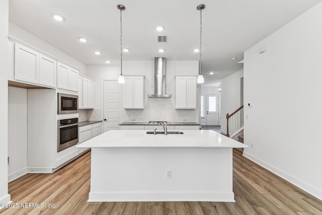 kitchen featuring an island with sink, oven, wall chimney range hood, black microwave, and a sink