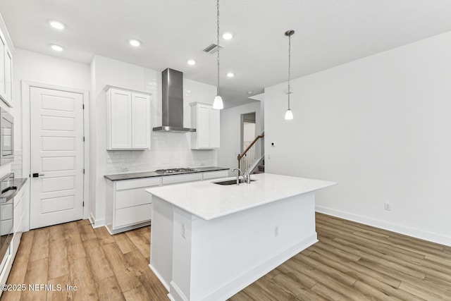 kitchen featuring light wood finished floors, wall chimney range hood, a sink, and stainless steel gas stovetop