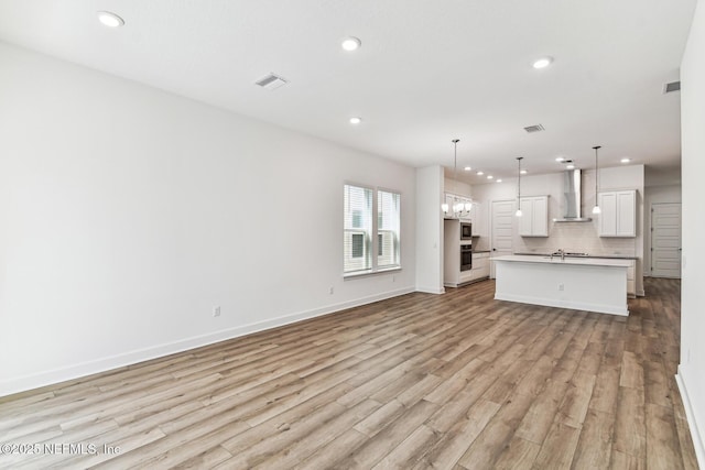 unfurnished living room featuring baseboards, visible vents, a sink, and light wood finished floors