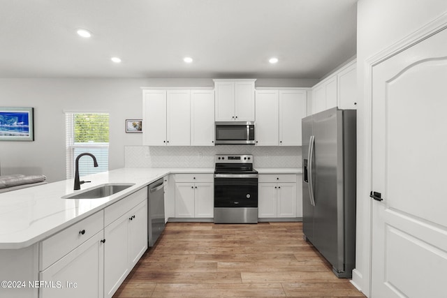 kitchen with kitchen peninsula, stainless steel appliances, sink, light hardwood / wood-style flooring, and white cabinetry