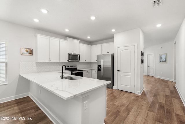 kitchen featuring wood-type flooring, kitchen peninsula, appliances with stainless steel finishes, light stone counters, and white cabinetry