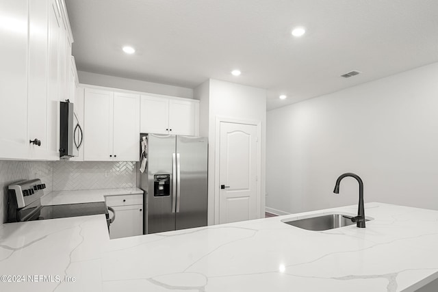 kitchen featuring light stone countertops, decorative backsplash, stainless steel appliances, sink, and white cabinetry