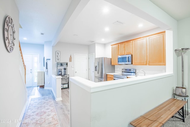 kitchen with kitchen peninsula, stainless steel appliances, light brown cabinets, beam ceiling, and light hardwood / wood-style flooring