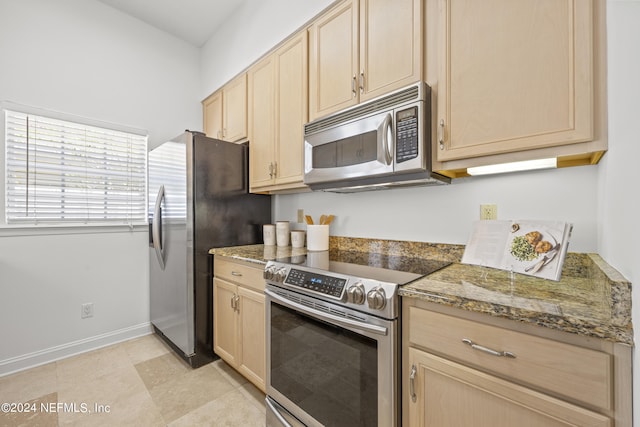 kitchen with light brown cabinets, stainless steel appliances, and dark stone counters