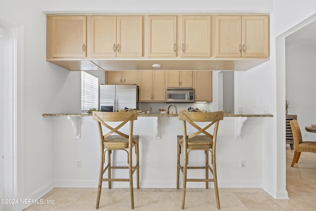 kitchen with a breakfast bar, light stone counters, light brown cabinetry, and appliances with stainless steel finishes