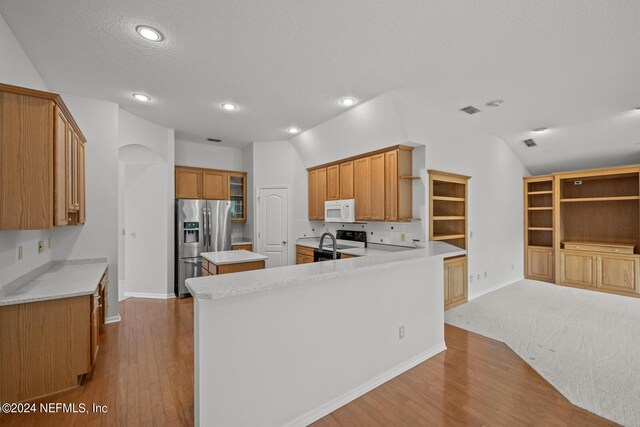 kitchen featuring lofted ceiling, white appliances, kitchen peninsula, backsplash, and light hardwood / wood-style floors