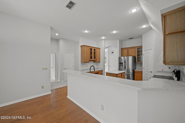 kitchen with range, kitchen peninsula, backsplash, light hardwood / wood-style floors, and stainless steel fridge with ice dispenser