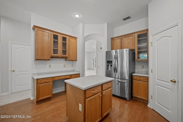 kitchen featuring stainless steel fridge with ice dispenser, a center island, wood-type flooring, and built in desk