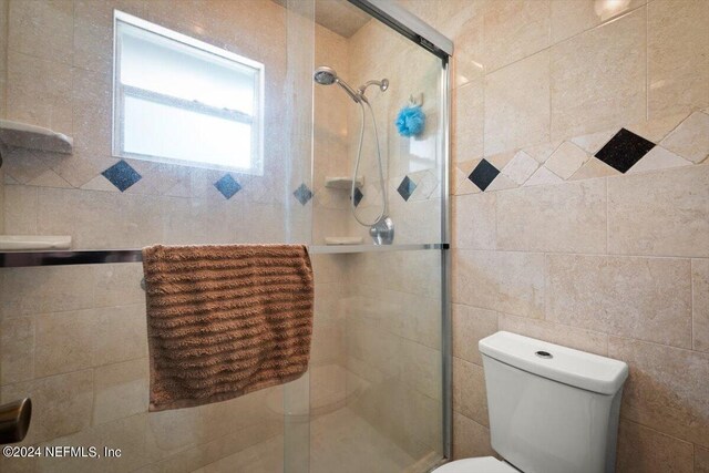 bathroom featuring a shower with door, toilet, and tile walls