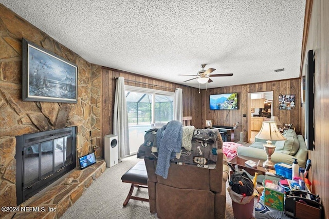 carpeted living room featuring a textured ceiling, wooden walls, ceiling fan, and a fireplace