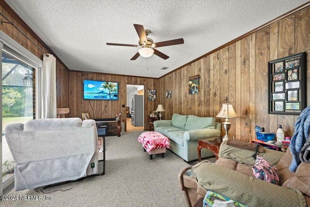 living room with ceiling fan, carpet floors, crown molding, a textured ceiling, and wooden walls