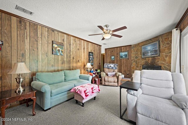 carpeted living room with wood walls, ceiling fan, and a textured ceiling