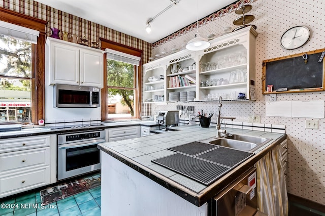 kitchen with tile patterned floors, rail lighting, appliances with stainless steel finishes, tile counters, and white cabinetry