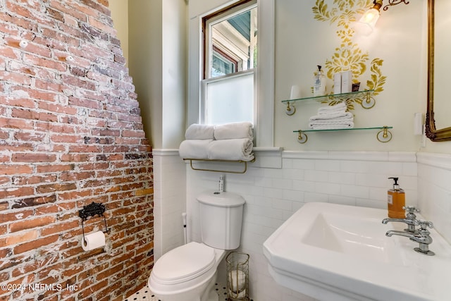 bathroom with toilet, sink, and brick wall