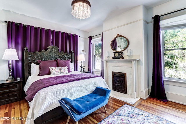 bedroom with a brick fireplace, an inviting chandelier, multiple windows, and light hardwood / wood-style flooring