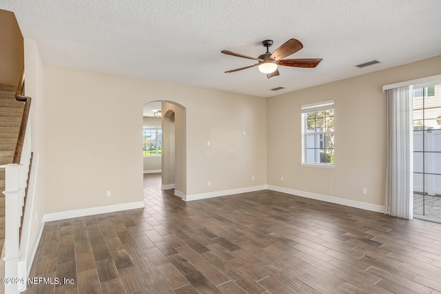 unfurnished room with stairway, visible vents, a wealth of natural light, and dark wood-type flooring