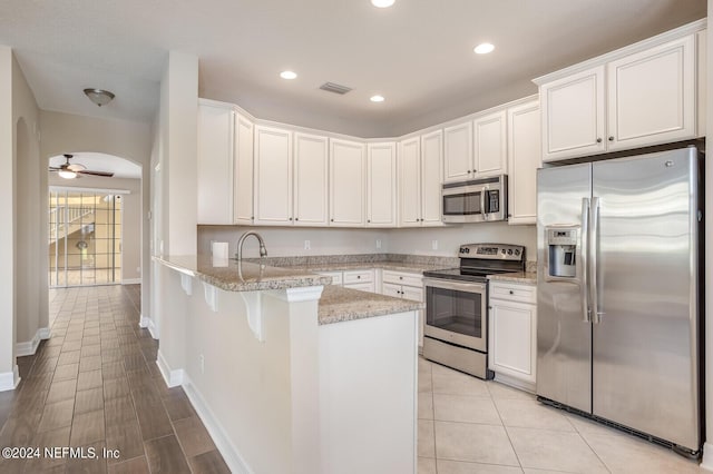 kitchen featuring arched walkways, stainless steel appliances, a peninsula, a ceiling fan, and white cabinetry