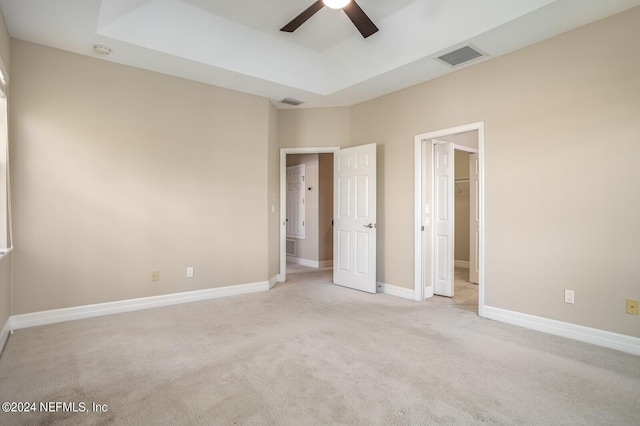 unfurnished bedroom featuring a walk in closet, a raised ceiling, visible vents, carpet flooring, and baseboards