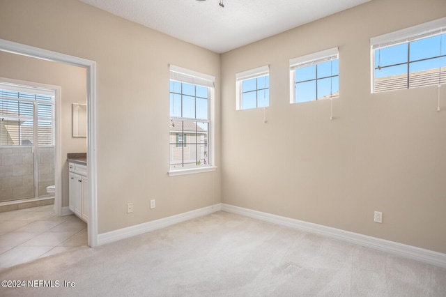 unfurnished bedroom with ensuite bath, baseboards, a textured ceiling, and light colored carpet