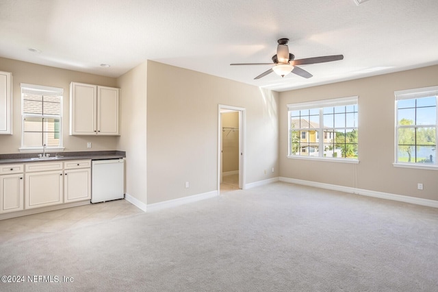 kitchen featuring white dishwasher, light colored carpet, a sink, baseboards, and dark countertops