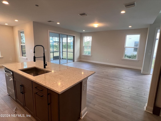 kitchen with light stone countertops, light hardwood / wood-style flooring, a kitchen island with sink, and sink