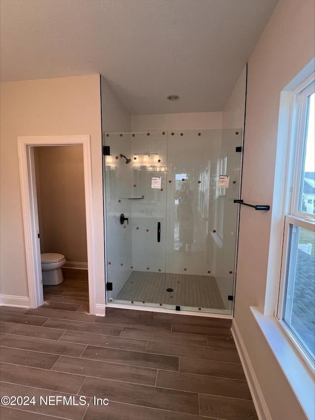 bathroom with hardwood / wood-style flooring, toilet, and a shower with shower door