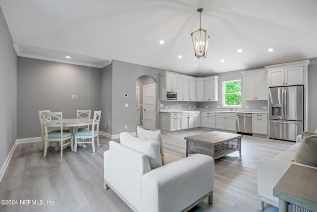 living room with sink, ornamental molding, a notable chandelier, and light wood-type flooring