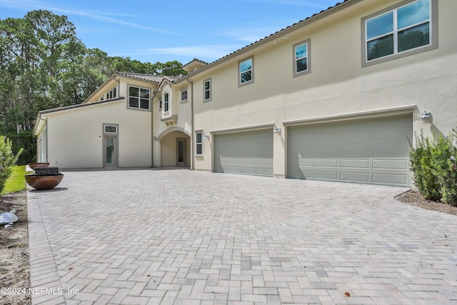 view of front of house with a garage, decorative driveway, a tiled roof, and stucco siding