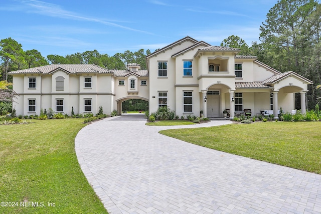 mediterranean / spanish-style home featuring a tiled roof, decorative driveway, a front yard, and stucco siding