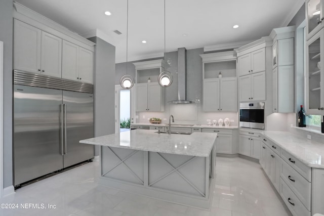 kitchen featuring a center island with sink, wall chimney exhaust hood, decorative light fixtures, light stone counters, and stainless steel appliances