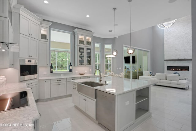 kitchen featuring a center island with sink, hanging light fixtures, a large fireplace, white cabinetry, and stainless steel appliances