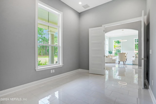 tiled spare room with visible vents, arched walkways, and baseboards