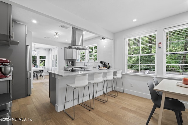 kitchen with kitchen peninsula, a kitchen bar, island exhaust hood, light hardwood / wood-style flooring, and gray cabinets