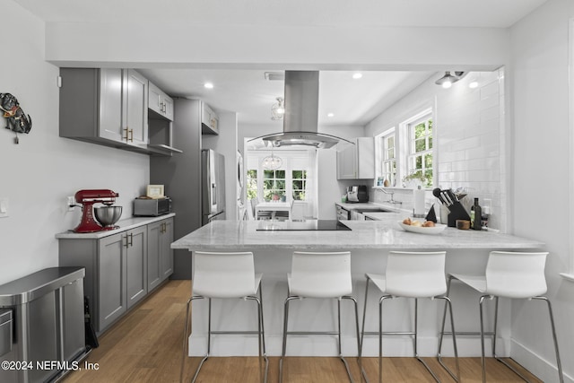 kitchen with gray cabinetry, island range hood, kitchen peninsula, and stainless steel refrigerator with ice dispenser