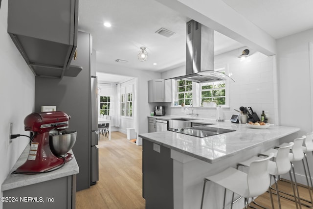 kitchen featuring island exhaust hood, black electric stovetop, a kitchen bar, kitchen peninsula, and gray cabinetry