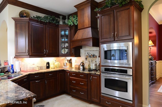 kitchen featuring premium range hood, appliances with stainless steel finishes, tasteful backsplash, light stone countertops, and sink