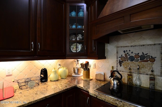 kitchen with light stone countertops, dark brown cabinetry, black electric stovetop, backsplash, and custom range hood