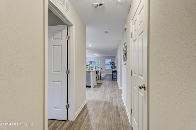 corridor with a textured ceiling and light hardwood / wood-style flooring