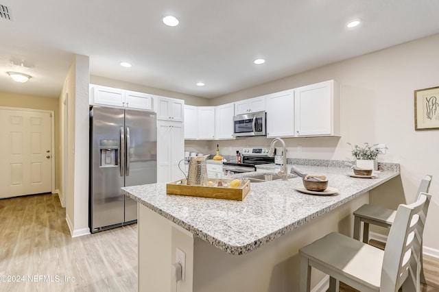 kitchen with kitchen peninsula, a breakfast bar, stainless steel appliances, sink, and white cabinetry